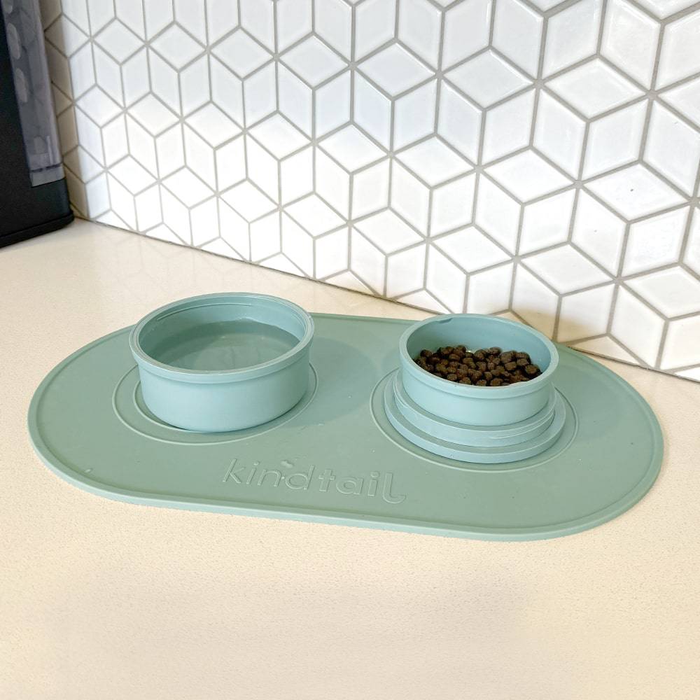 green silicone dog food mat and bowls on the counter in a white tile back drop