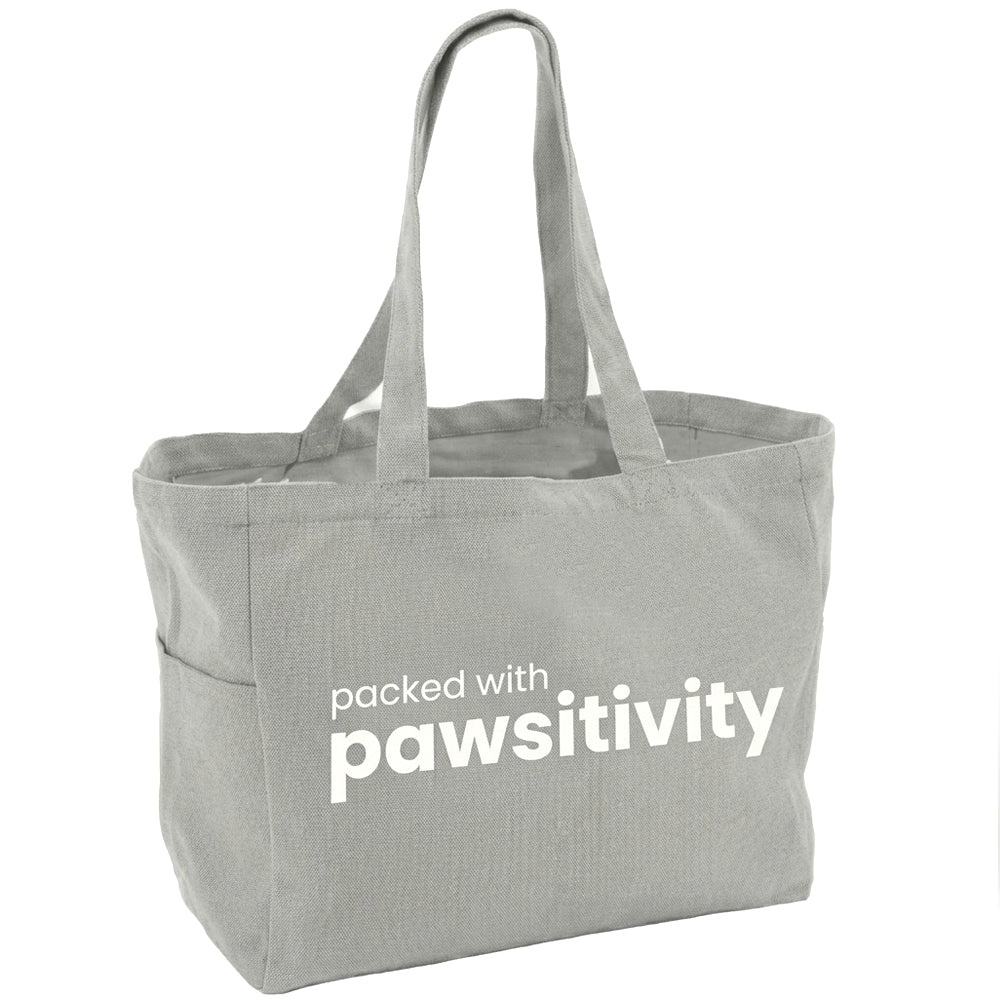 Large beige tote bag with "Pawsitivity" printed on the front, featuring dog paw prints and sturdy handles, by KindTail.